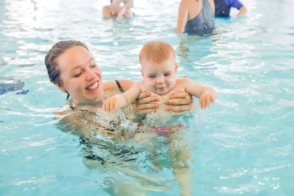 A smiling mother holding a small baby in the swimming pool for a swimming lesson