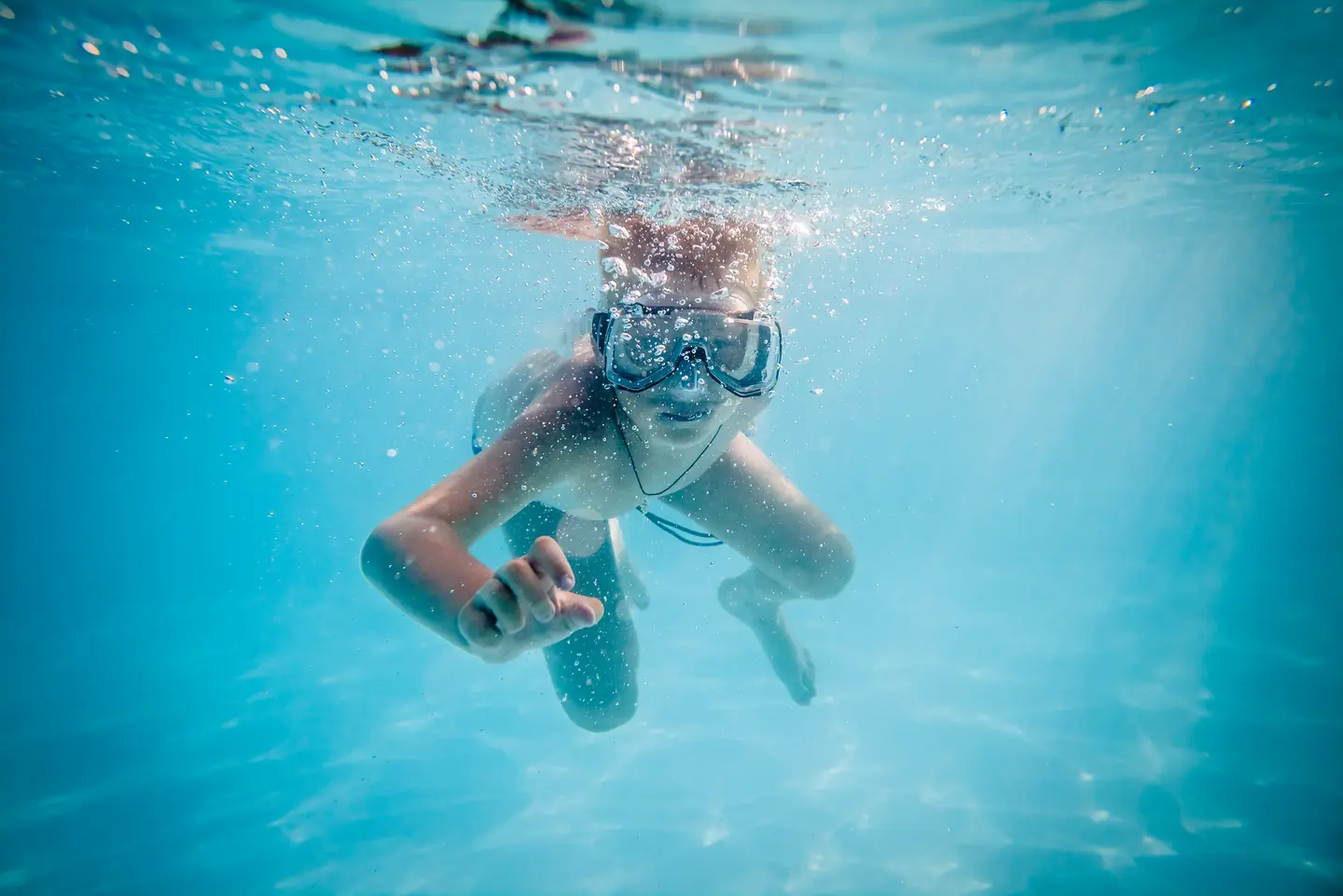A teenage boy swimming underwater with his goggles on