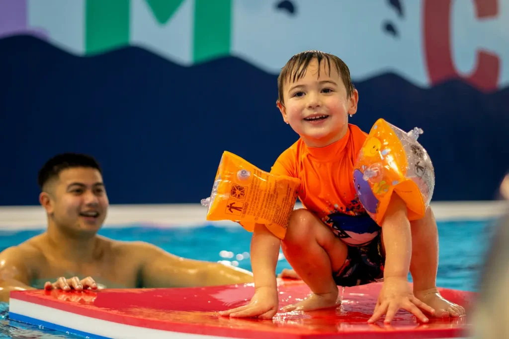 A young boy with armbands standing on a float being pushed by his dad