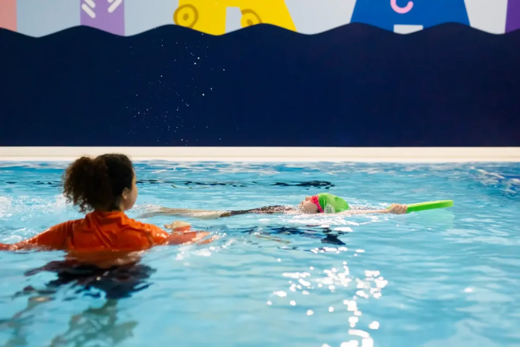 Child and swimming instructor practicing backstroke with a float