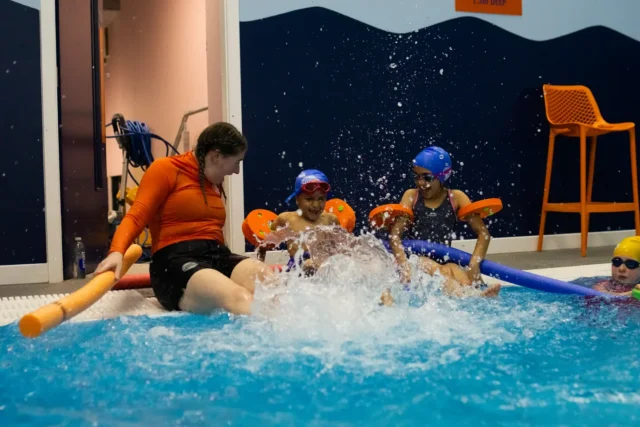 Kids and their swimming teacher splashing and having fun in the water