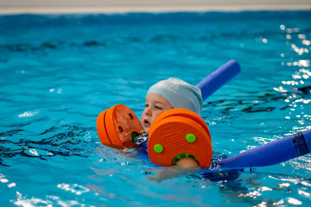 A little baby boy swimming with arm bands and a pool noodle