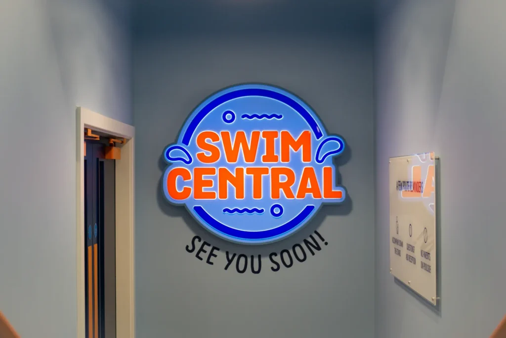A fancy neon wall sign with the swim central logo and See you soon text below.